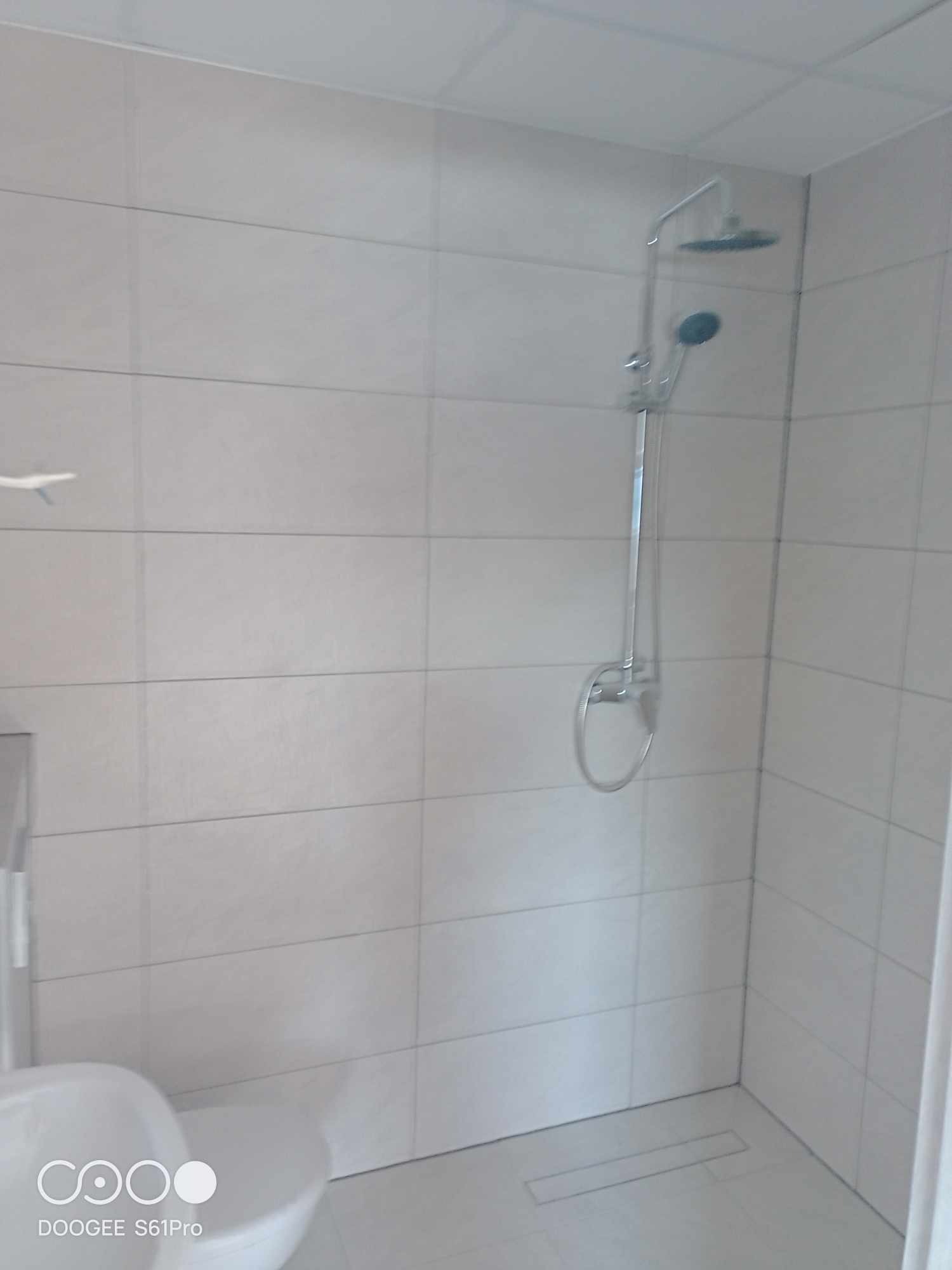 Jasna łazienka z kabiną prysznicową typu walk-in, wykończona białymi, prostokątnymi płytkami i odpływem liniowym w podłodze.