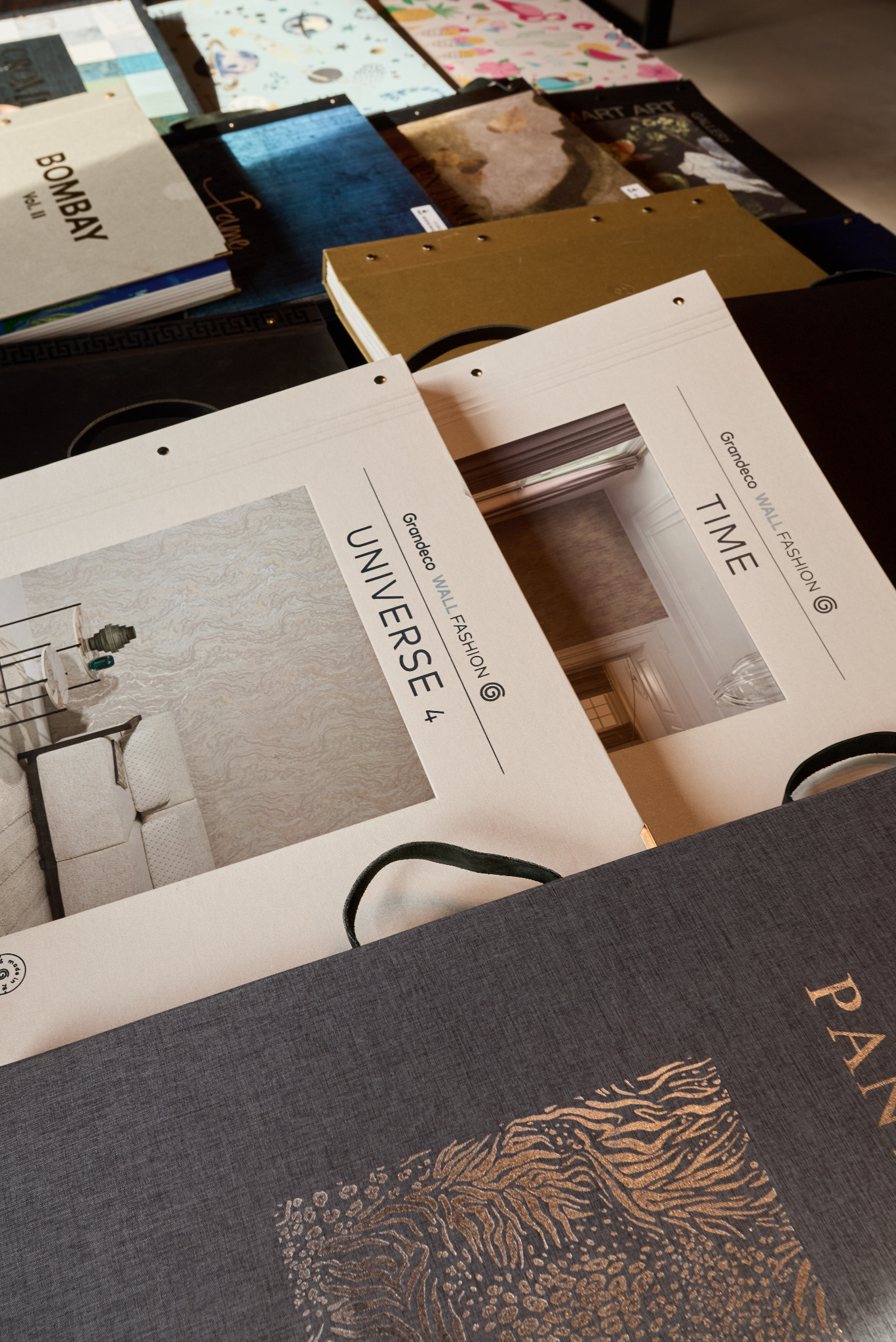 Katalogi z wzorami tapet Grandeco Wall Fashion: Universe 4 i Time, ułożone na stole, prezentują różnorodność stylów i faktur. Detaliczny widok na kolekcje.