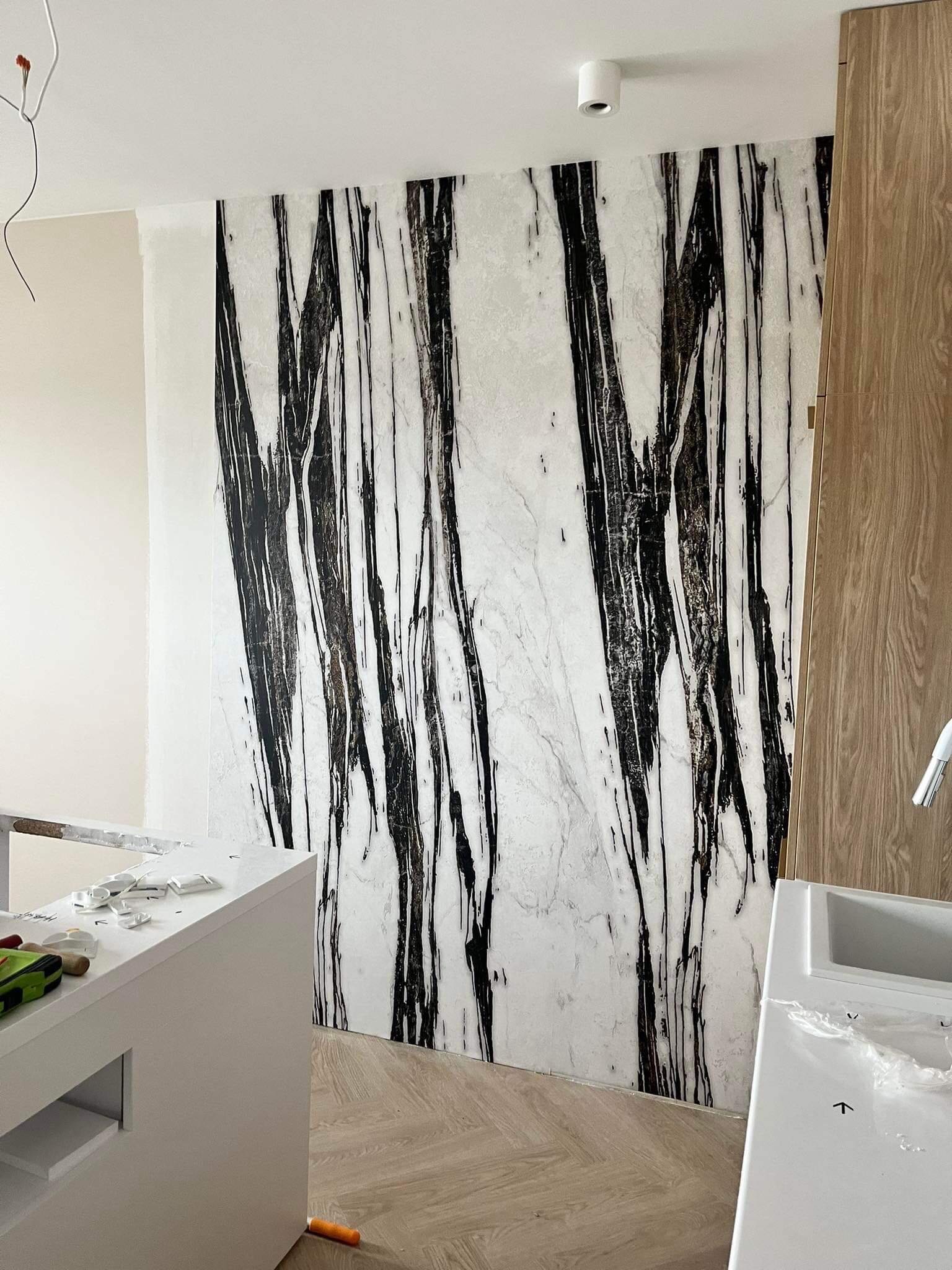 Ściana wyłożona marmurowymi płytami z unikalnym wzorem czarnych żył, sąsiadująca z drewnianą zabudową, w trakcie prac wykończeniowych.