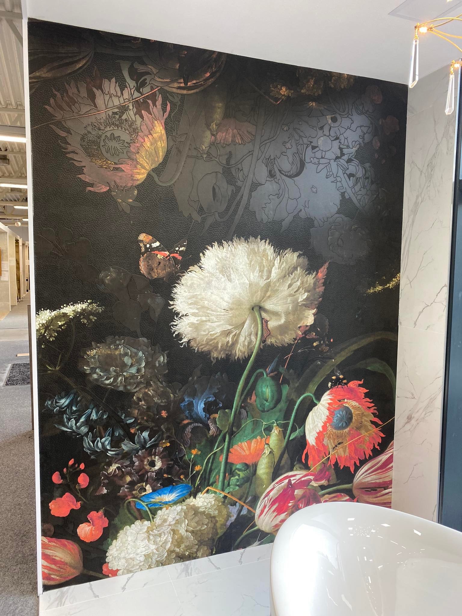 Tapeta w stylu holenderskiego malarstwa z motywem kwiatów i motyla, umieszczona na ścianie w łazience, obok marmurowych płytek i białej wanny.