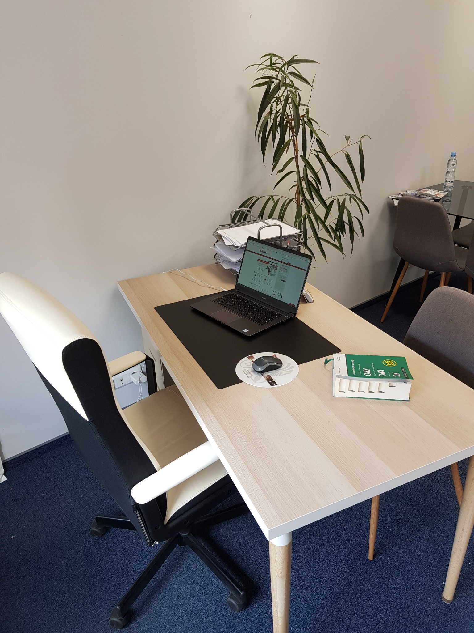 Biuro z biurkiem, laptopem, kodeksami prawnymi i rośliną doniczkową, nowoczesne krzesło biurowe z białymi elementami, minimalistyczny wystrój.