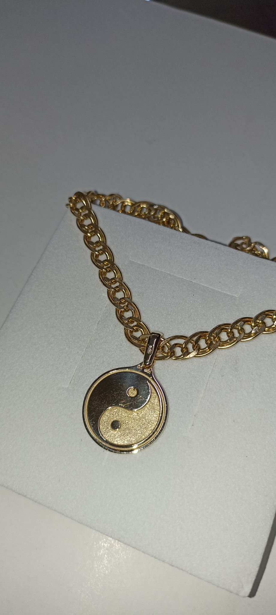 Złoty łańcuszek z zawieszką Yin Yang na białym tle, prezentowany na pudełku.