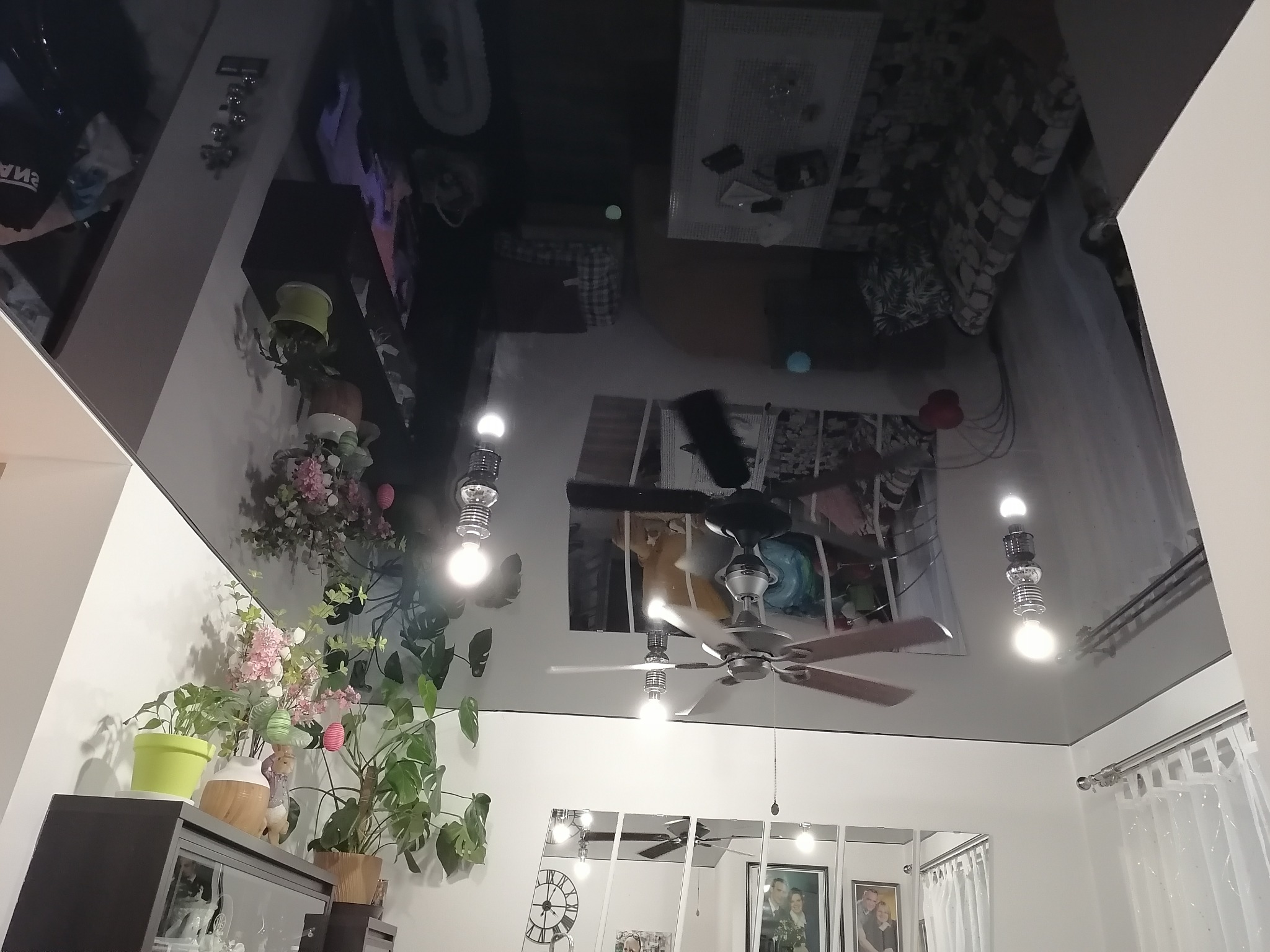 Błyszczący czarny sufit napinany z odbiciem wyposażenia pokoju, widoczne lampy dekoracyjne i fragment ściany z lustrami.