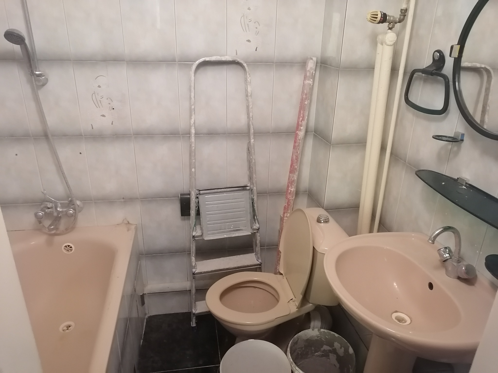 Łazienka w trakcie remontu: beżowa armatura, drabina malarska oparta o ścianę z resztkami farby, widoczne ślady po malowaniu na płytkach.