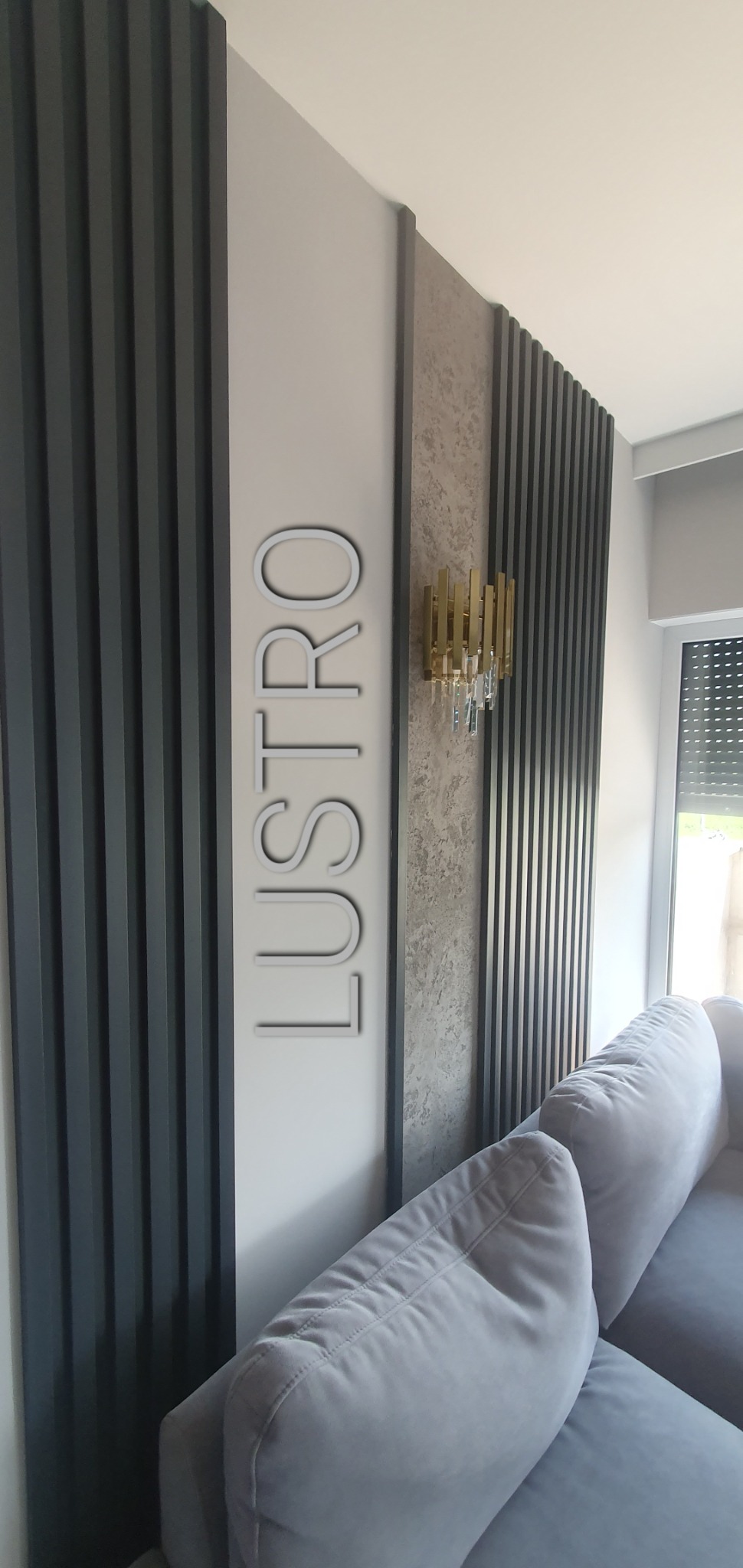 Szare lamele ścienne z napisem 'LUSTRO' i złotym kinkietem z kryształkami, widok z boku na fragment sofy.