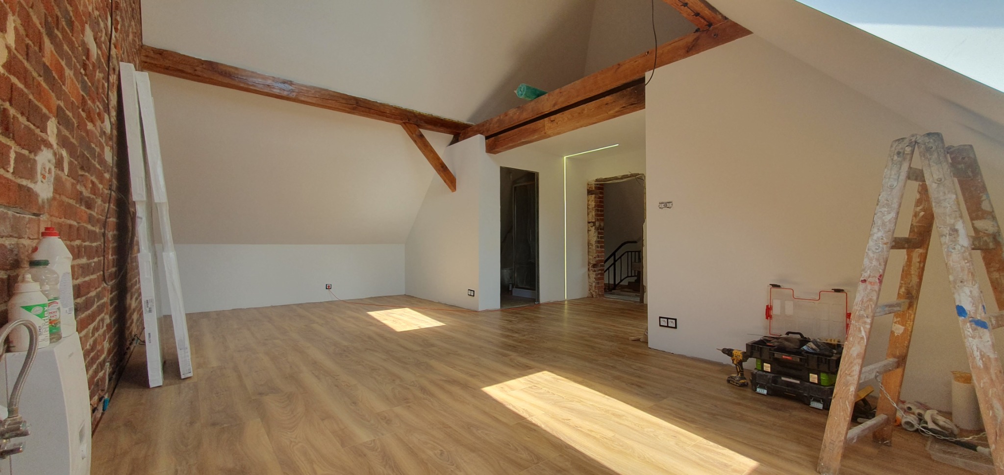 Poddasze w Zielonej Górze po remoncie, z drewnianymi belkami stropowymi, świeżo pomalowanymi ścianami, nową podłogą i widocznymi narzędziami oraz drabiną malarską.