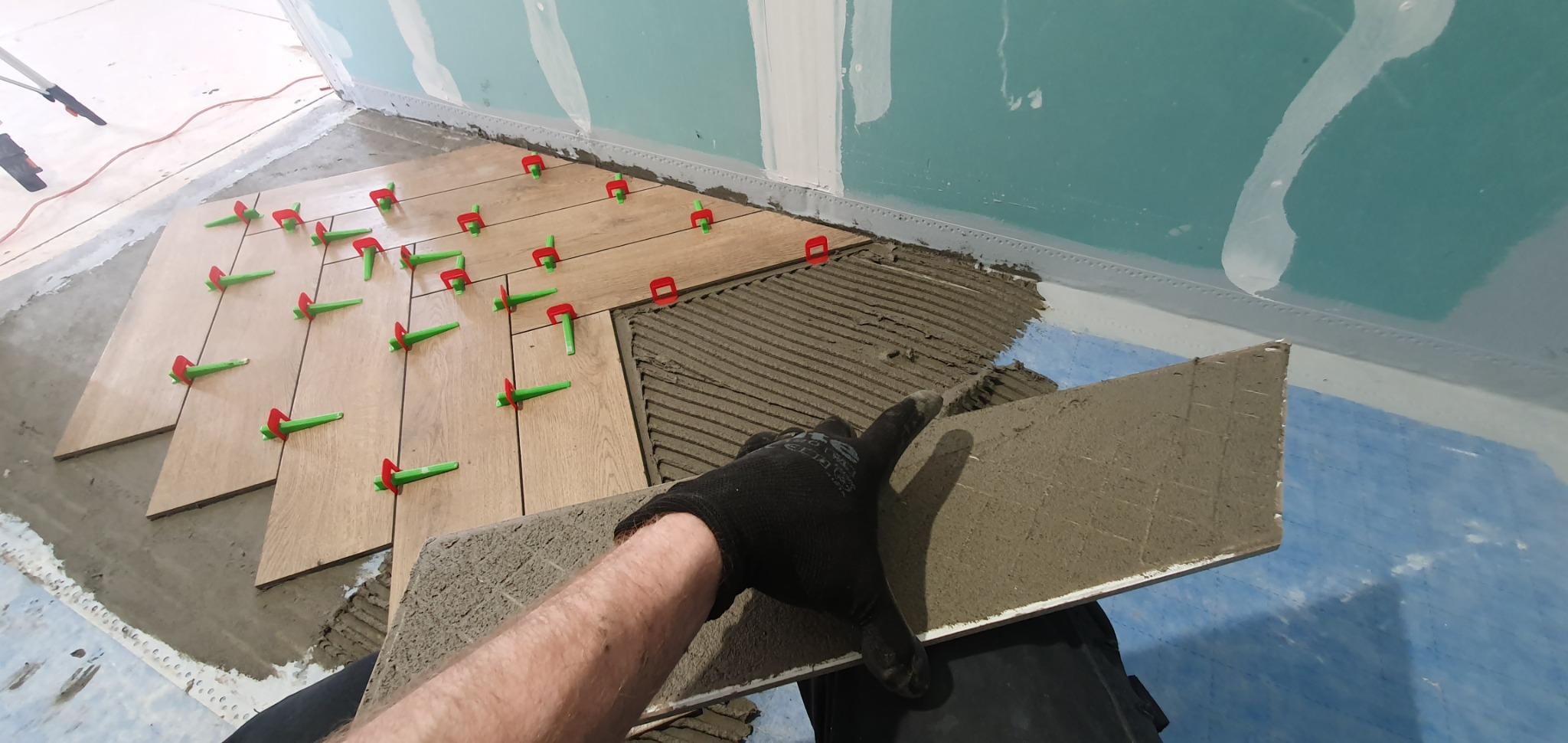 Układanie podłogi z płytek imitujących drewno, z użyciem klipsów poziomujących, widok z perspektywy osoby układającej.