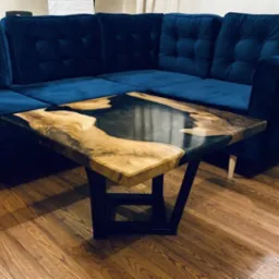 Stolik kawowy z blatem z drewna i żywicy epoksydowej, czarne metalowe nogi, na tle granatowej sofy i drewnianej podłogi.