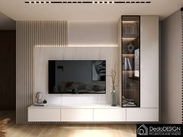 Nowoczesna ściana TV z białymi szafkami, marmurowym panelem i pionowymi listwami dekoracyjnymi, uzupełniona przeszkloną witryną z podświetleniem i elementami dekoracyjnymi.