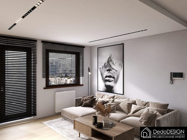 Nowoczesny salon z szarym narożnikiem, drewnianym stolikiem kawowym i czarno-białym portretem na ścianie, oświetlony liniowymi lampami LED w suficie.
