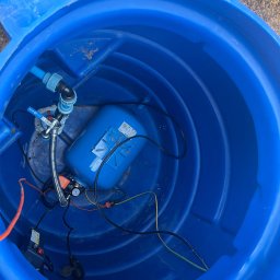 Wiercenie Studni Tadeusz Sadłowski - Wnętrze niebieskiej studni z hydroforem, zaworem i instalacją elektryczną, widok z góry.