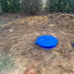 Niebieska pokrywa studni na wykopanym terenie, kable elektryczne wokół, przygotowanie do instalacji studni głębinowej w ogrodzie.