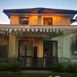 Zadaszony taras z przesuwnymi szklanymi ścianami, drewnianą podłogą i zewnętrznym oświetleniem, widoczny z zewnątrz, z drabiną opartą o jedną ze ścian, tuż po umyciu.