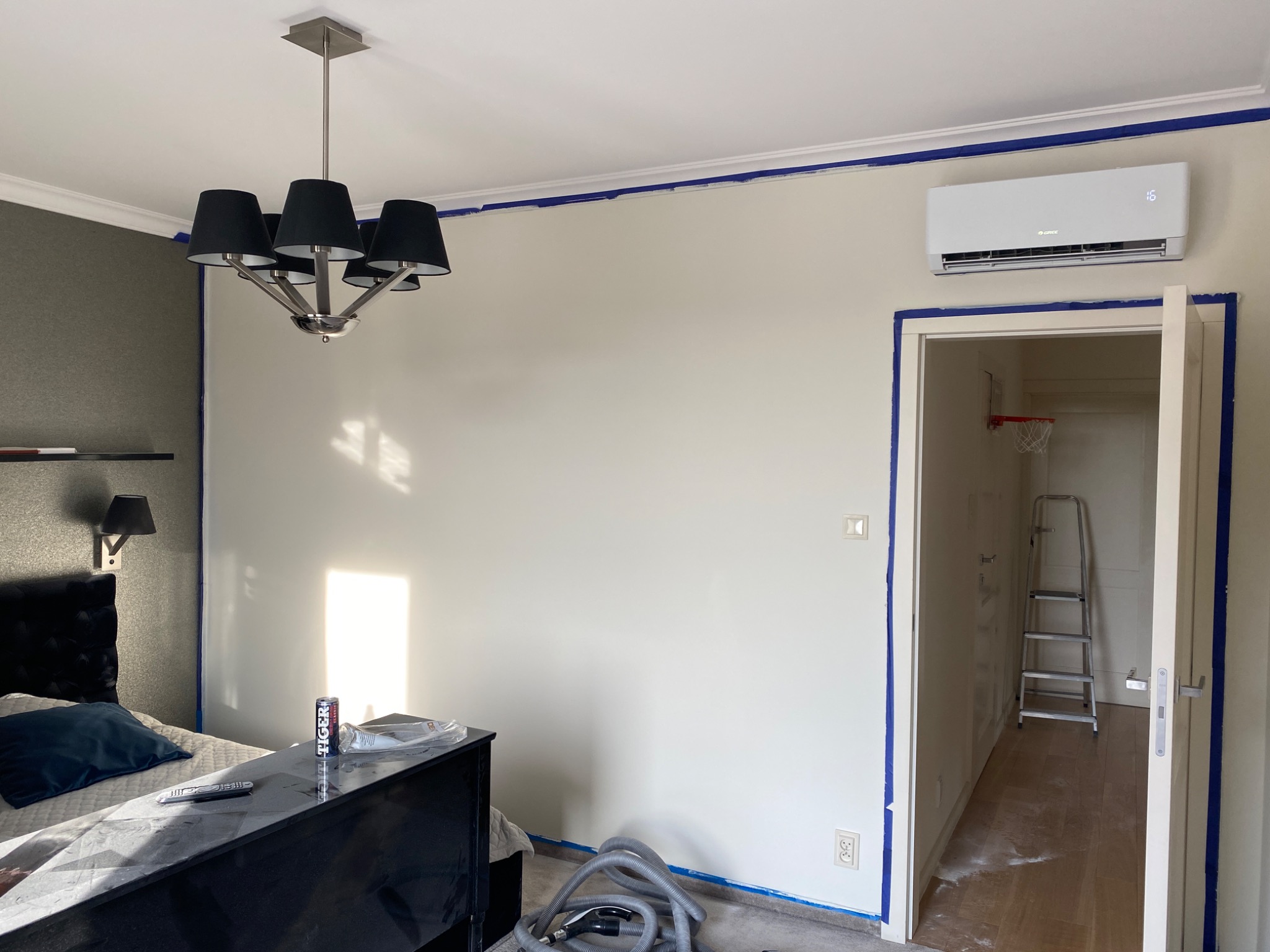 Pokój w trakcie malowania: ściany zabezpieczone taśmą malarską, widoczne ślady farby, w tle drabina i kosz do koszykówki.