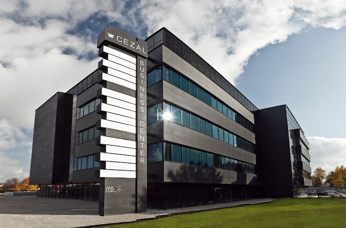 Nowoczesny budynek biurowy CEZAL Business Center z czarną elewacją i dużymi oknami, widoczny z zewnątrz w słoneczny dzień, z logo firmy na charakterystycznym pylonie.