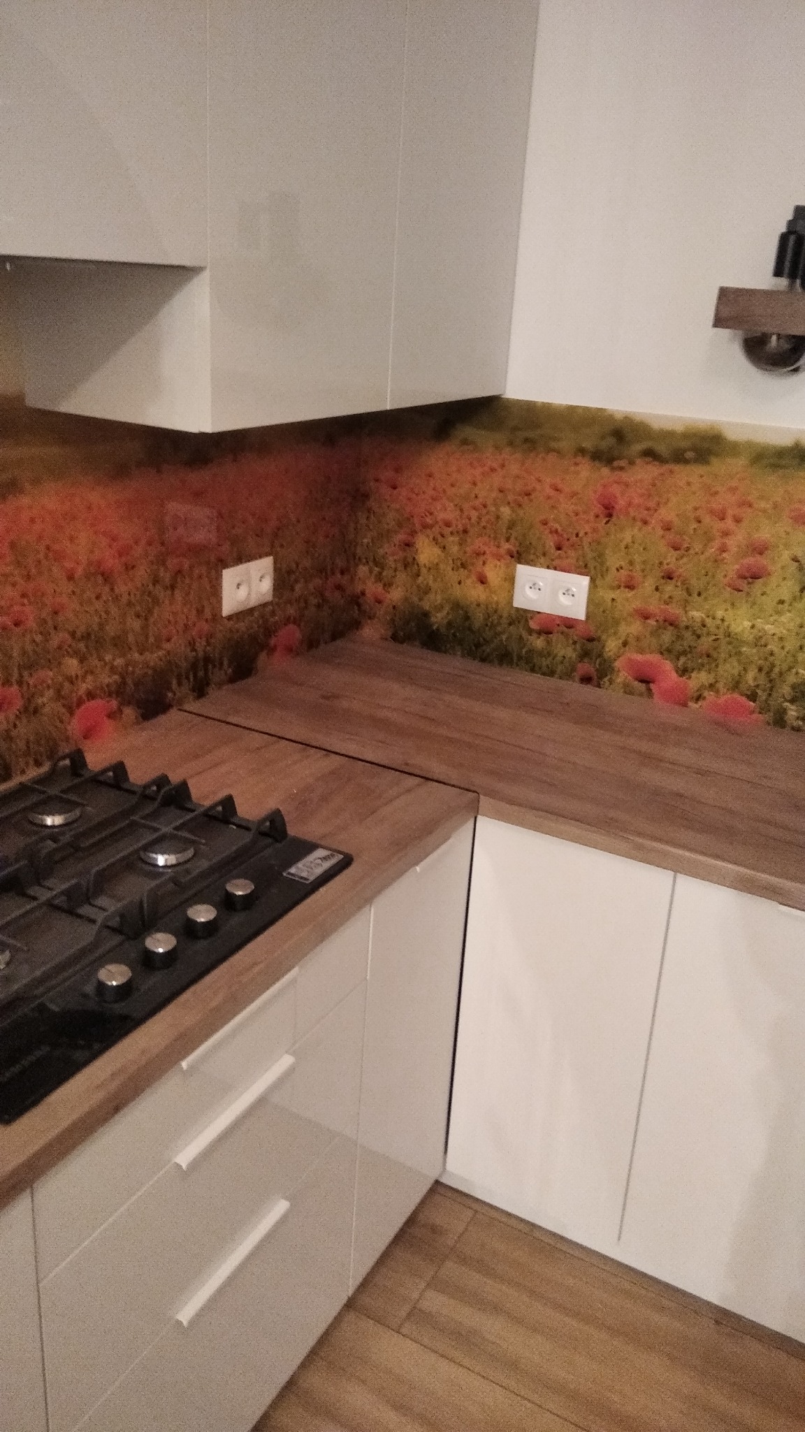 Kuchnia z płyta gazową i gniazdkami elektrycznymi na ścianie z motywem polnych maków.