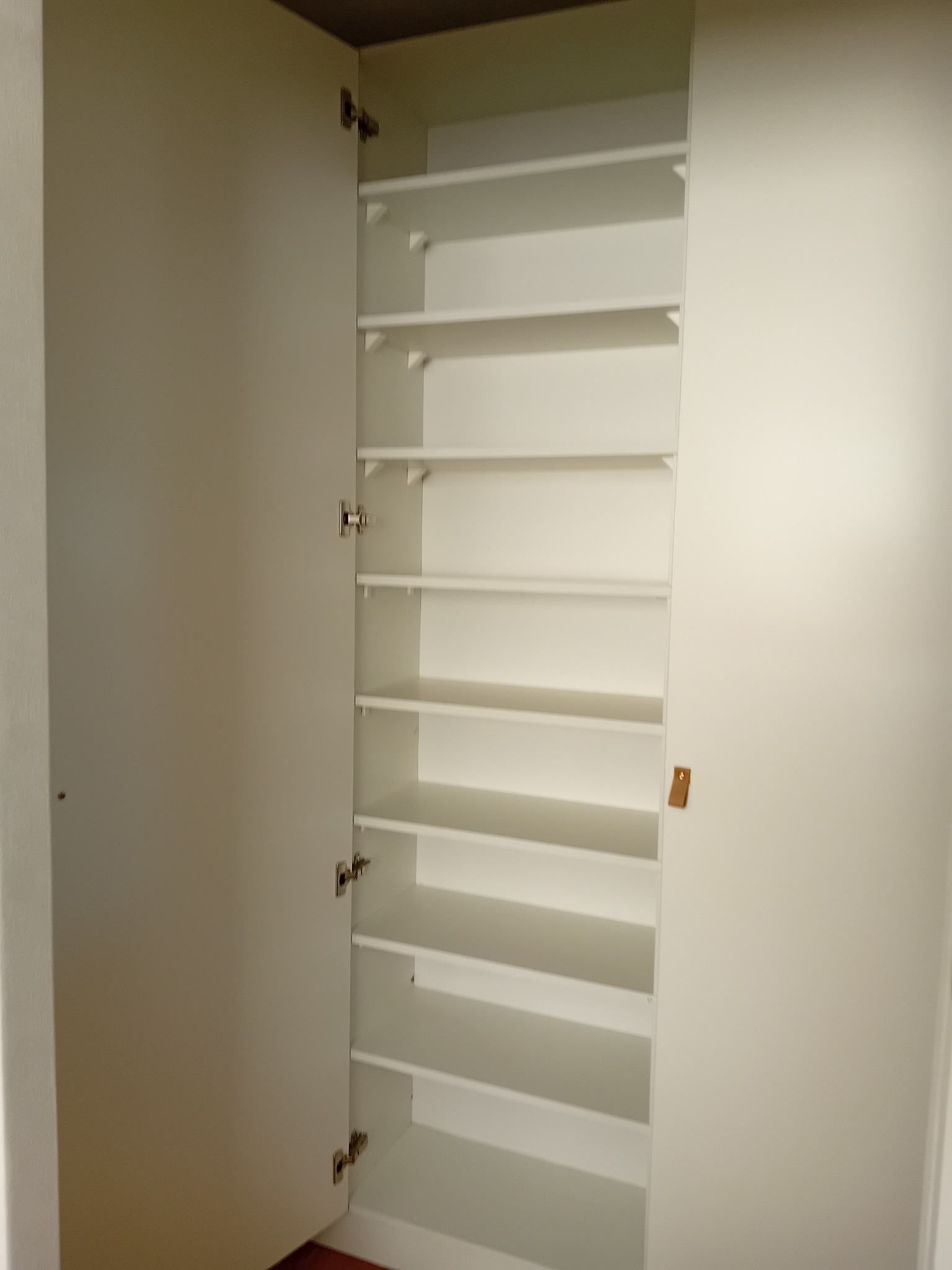 Wnętrze białej szafy z otwartymi drzwiami, widoczne liczne półki, metalowe zawiasy i skórzany uchwyt na drzwiach.