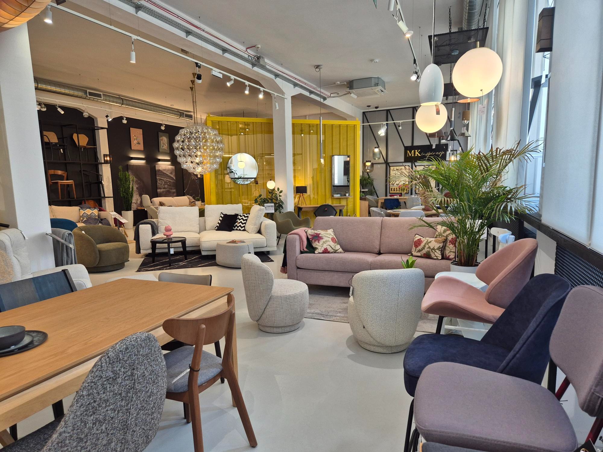 Salon meblowy w Gdańsku prezentuje różnorodne sofy, krzesła i stoły. Widoczne lampy wiszące, rośliny doniczkowe i elementy dekoracyjne. Aranżacja wnętrza.