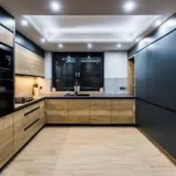 Nowoczesna kuchnia w kształcie litery U z frontami szafek w kolorze jasnego drewna i grafitu, czarnym blatem i oświetleniem LED podszafkowym oraz sufitowym.