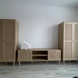 Dwie szafy i szafka RTV z frontami z plecionki rattanowej w surowym wnętrzu, na szafce leży biała torba z zakupami.