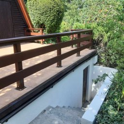 Piotr - Zadaszony taras z brązową balustradą i schodami prowadzącymi do piwnicy, otoczony zielenią.