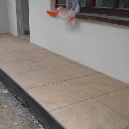 Piotr - Wykończony taras z beżowych płytek ceramicznych, widoczne detale listwy krawędziowej i fragment elewacji z oknem zabezpieczonym folią malarską.
