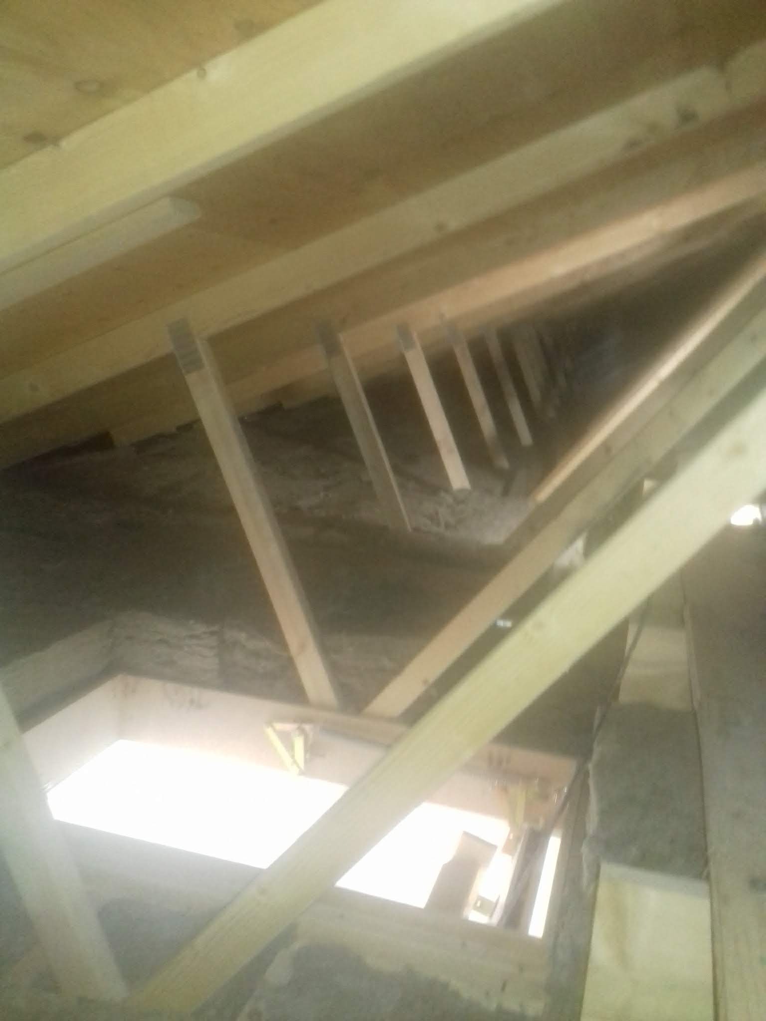 Szkielet drewnianej konstrukcji poddasza z widoczną izolacją i oknem dachowym, w trakcie budowy.