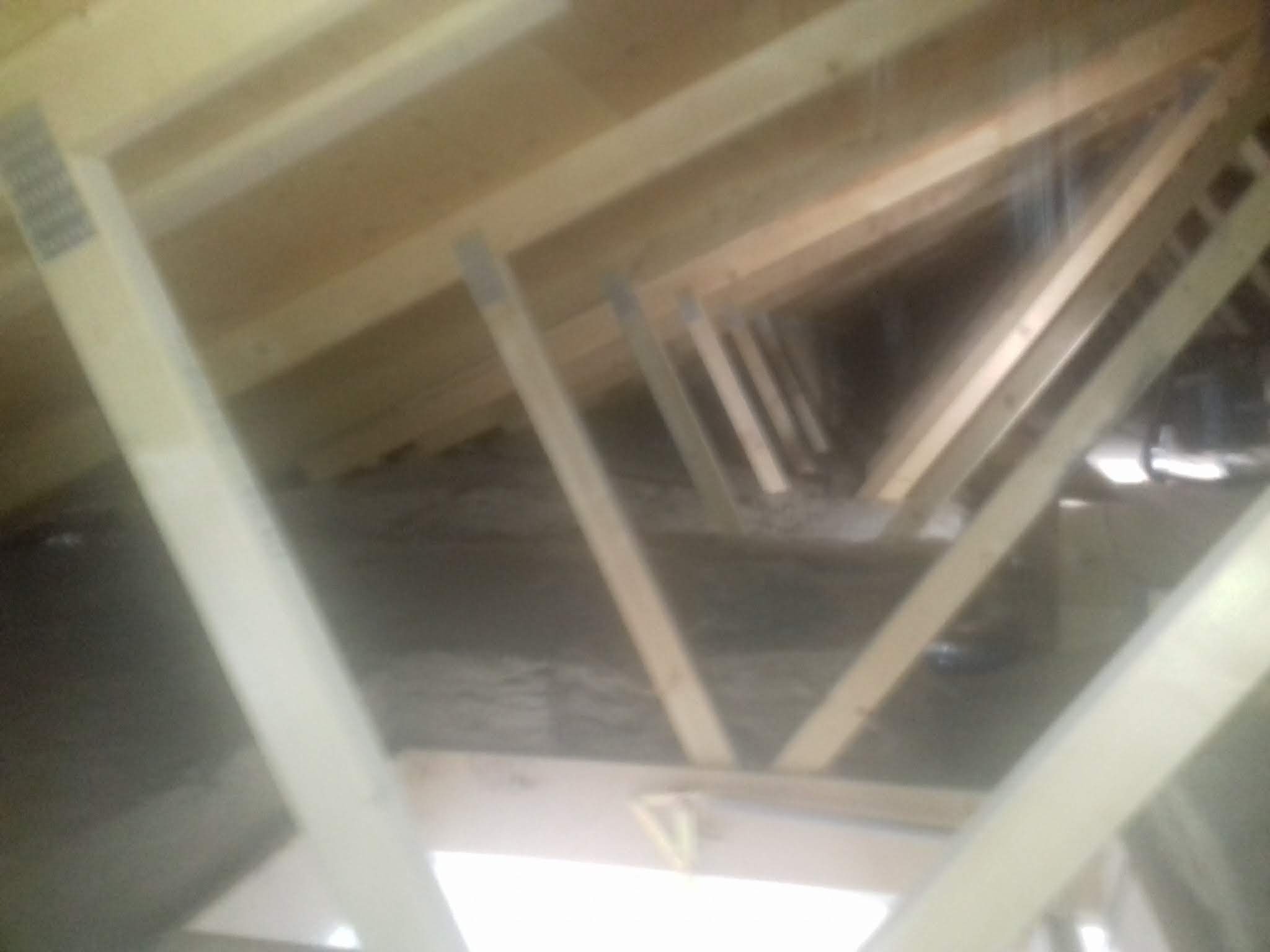 Drewniana konstrukcja dachu od wewnątrz, widoczne krokwie i izolacja, ujęcie od dołu w słabym oświetleniu.