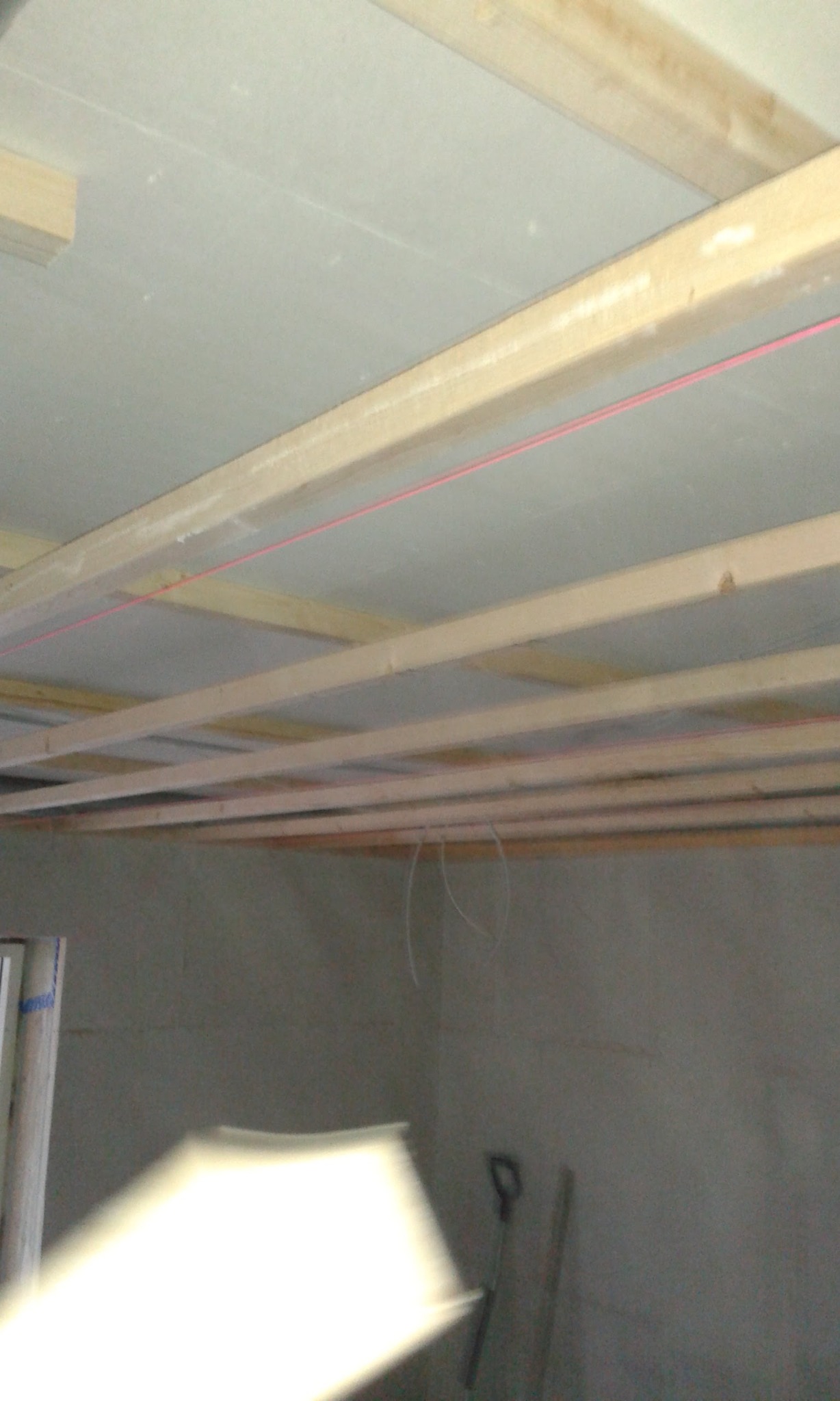 Konstrukcja drewniana podwieszanego sufitu z płyt kartonowo-gipsowych, widoczna czerwona nić laserowa wyznaczająca poziom, narzędzia opierają się o ścianę w tle.