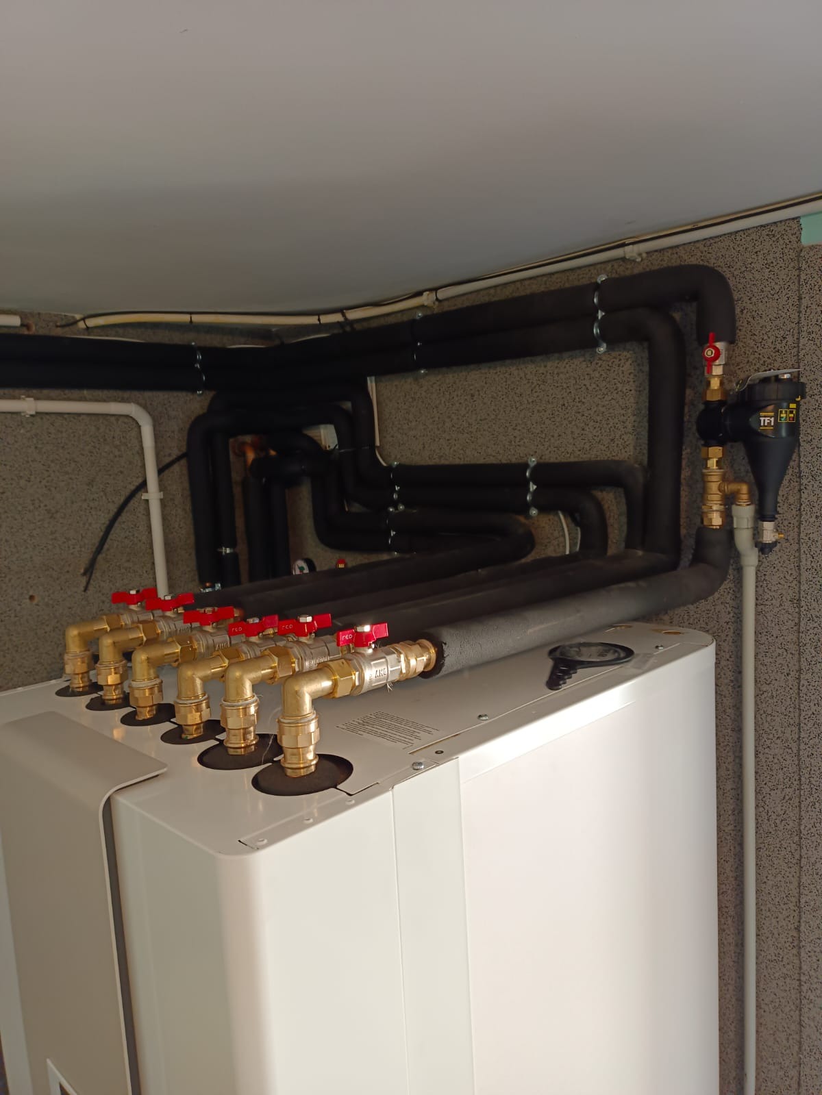 Kotłownia z pompą ciepła monoblok Stiebel Eltron typu powietrze-woda; widoczne rury w izolacji, zawory z czerwonymi pokrętłami oraz filtr. Centrala all in one zintegrowana z pompą drugiej strefy...