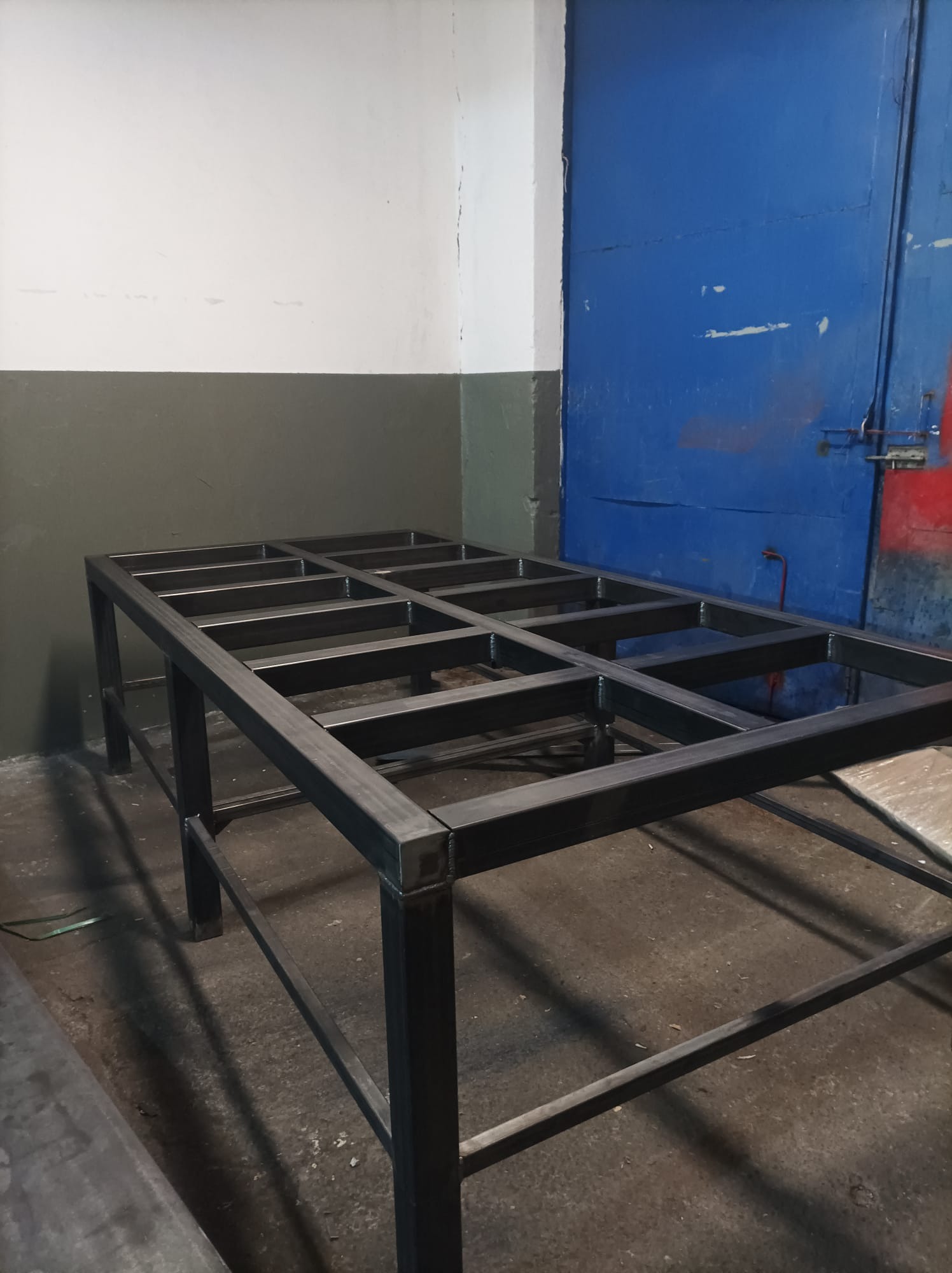 Metalowa konstrukcja szkieletowa hali w trakcie budowy, widoczna na tle ściany i niebieskich drzwi.