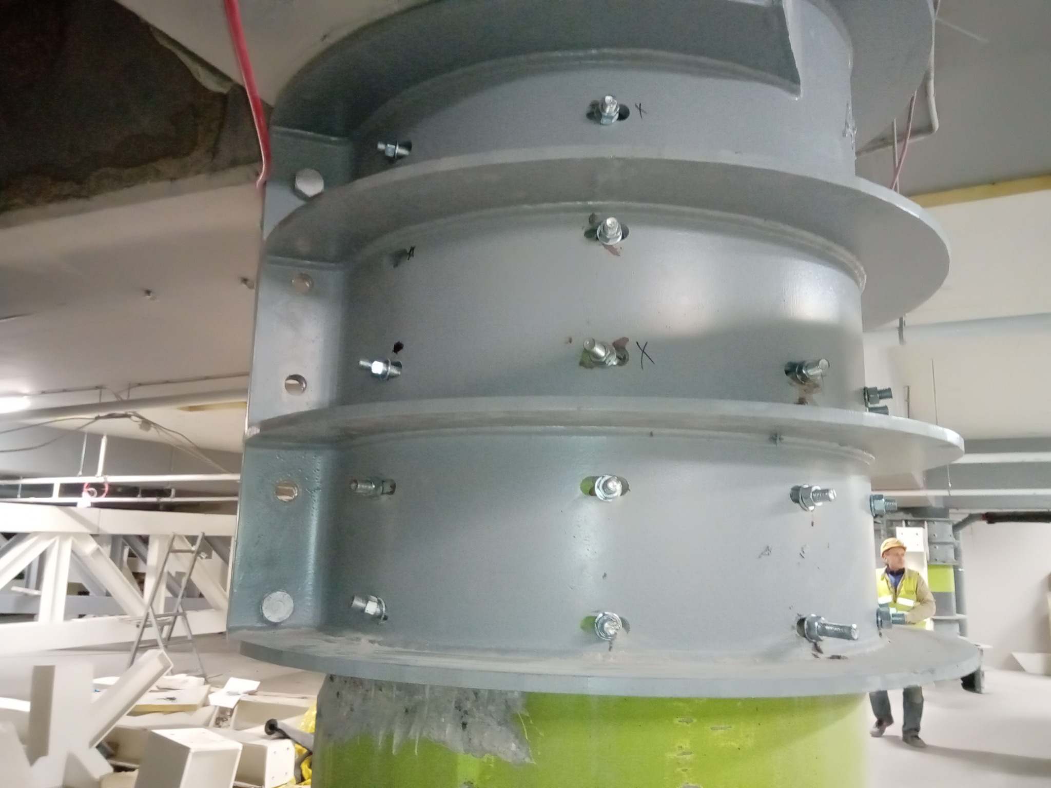 Wielkogabarytowa, stalowa konstrukcja kolumnowa, skręcana na śruby, widoczna w trakcie montażu wewnątrz budynku, pracownik w kasku w tle.