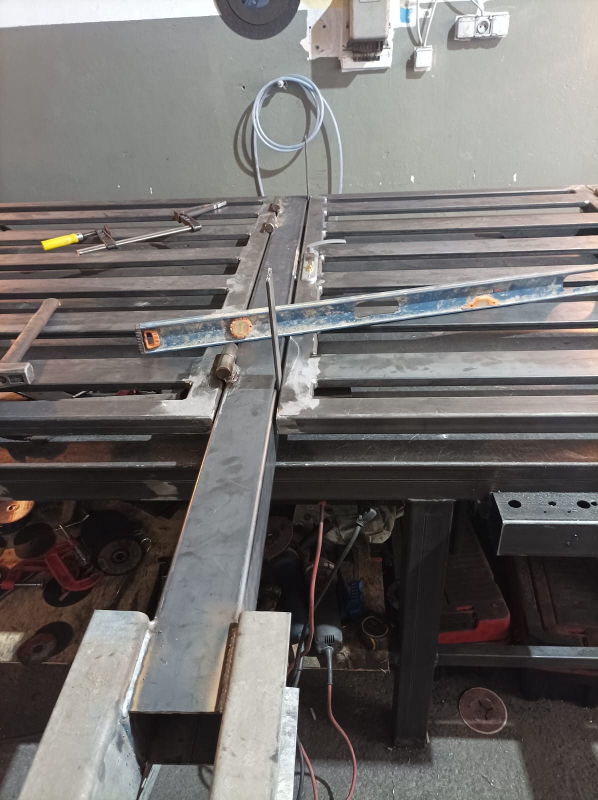 Metalowa konstrukcja spawana na stole warsztatowym, poziomica i narzędzia w tle, widoczne ślady spawania.