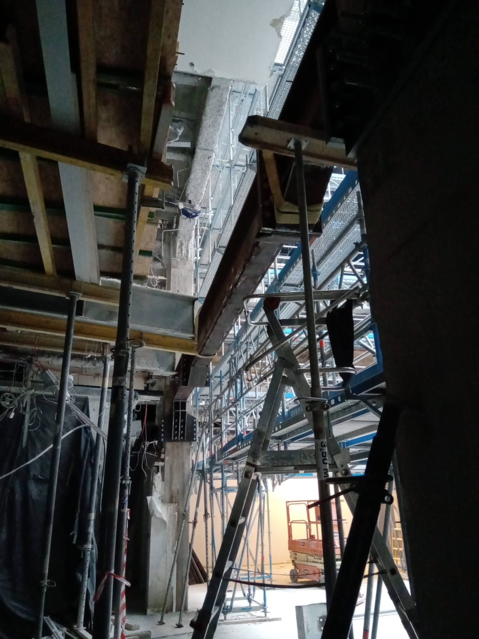 Konstrukcja stalowa hali w trakcie budowy we Wrocławiu, widoczne rusztowania, podpory stalowe, elementy drewniane szalunku oraz podnośnik nożycowy w tle.