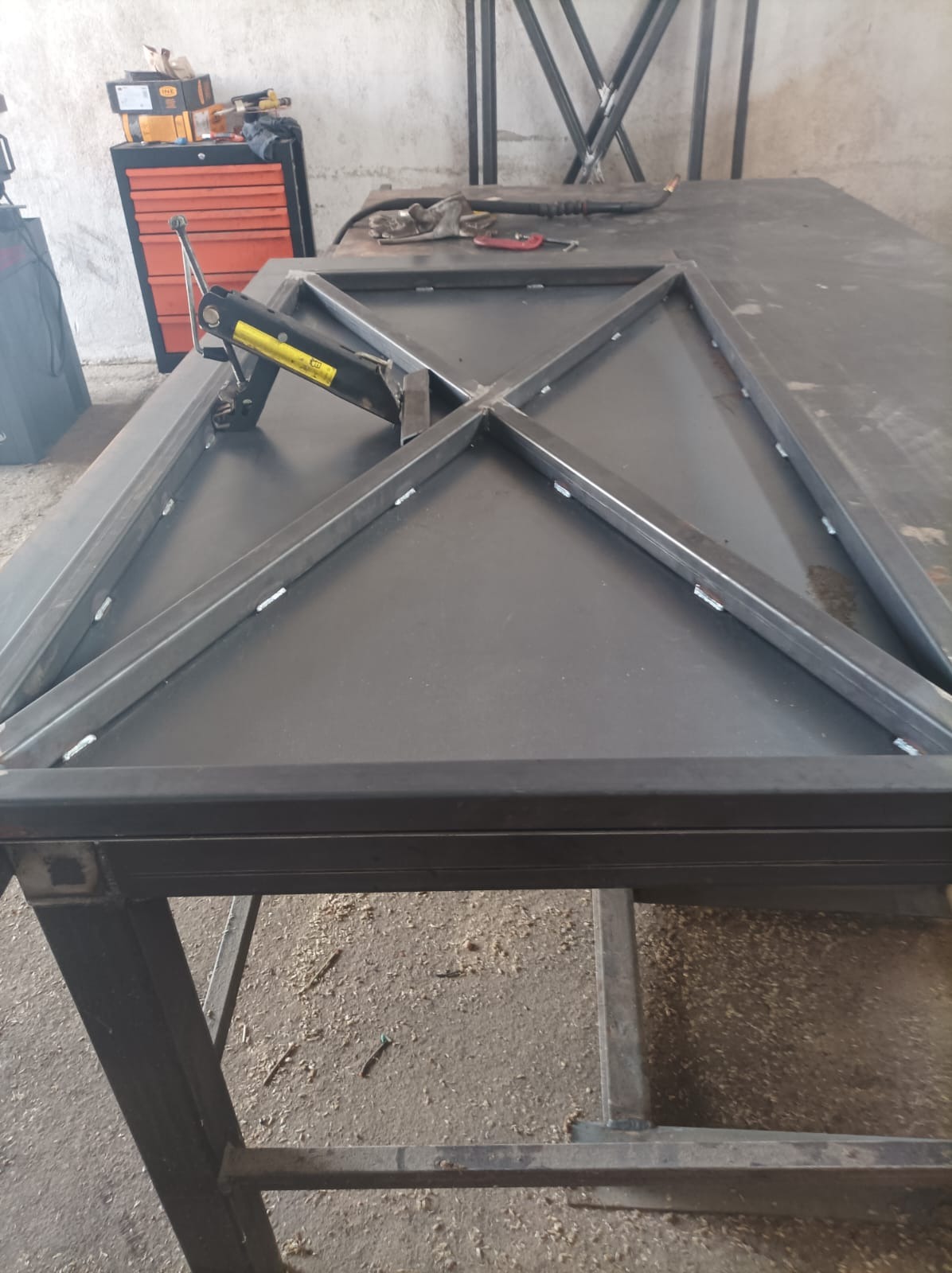 Konstrukcja stalowa z profili zamkniętych spawana na stole warsztatowym, widoczne ślady spawania, zacisk stolarski i narzędzia w tle.