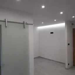 Wnętrze po remoncie: przesuwne, szklane drzwi z metalowym prowadzeniem, białe ściany z punktowym oświetleniem sufitowym i drewnopodobna podłoga.