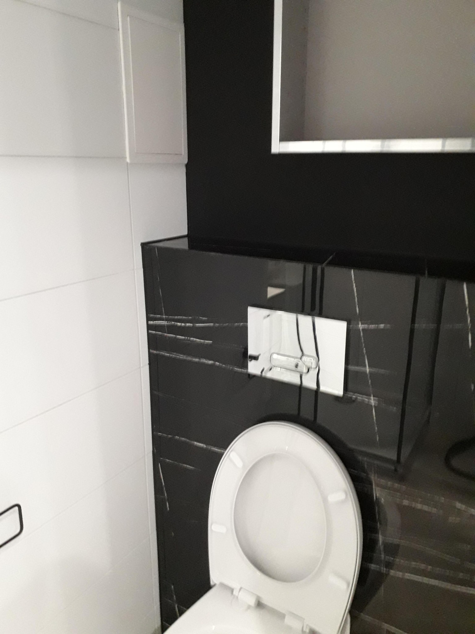 Nowoczesna toaleta podwieszana z czarnym marmurem i białymi płytkami w łazience w Szepietowie.