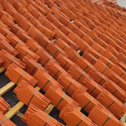 Mykhailo Mazuryk - Ułożone dachówki ceramiczne w pakietach, zabezpieczone zieloną taśmą, czekają na montaż na konstrukcji dachu. Widoczne drewniane łaty i membrana dachowa.