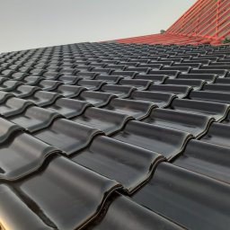 Mykhailo Mazuryk - Błyszczące, czarne dachówki ceramiczne ułożone na dachu. W tle widoczna czerwona konstrukcja więźby dachowej. Ujęcie z dołu, podkreślające regularność wzoru.