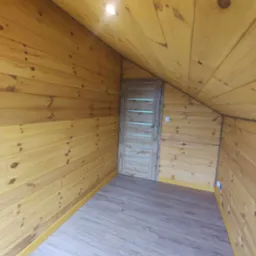 Wnętrze poddasza wykończonego boazerią w odcieniach ż&oacute;łci, z drewnianą podłogą imitującą panele i jasnymi drzwiami z poziomymi przeszkleniami, widoczne gniazdka elektryczne.