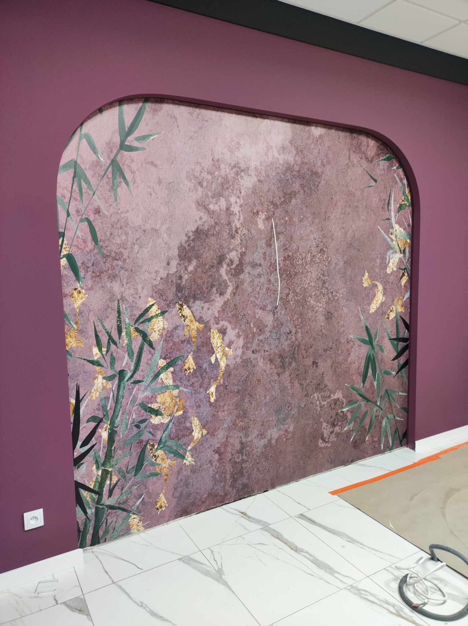 Ściana w kolorze śliwkowym z wnęką w kształcie łuku, wykończona tapetą z motywem bambusa i złotych rybek, biała podłoga z marmurowym wzorem, widoczne zabezpieczenia podłogi.
