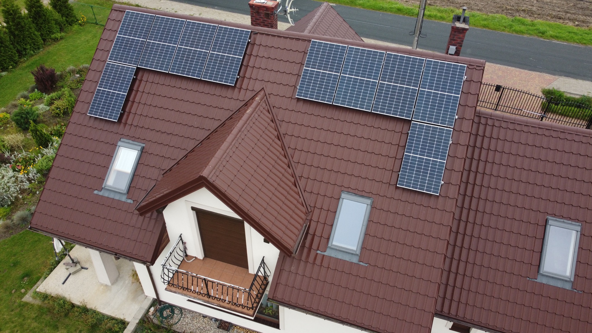 Widok z góry na brązowy dach domu z zamontowanymi panelami fotowoltaicznymi i oknami dachowymi.