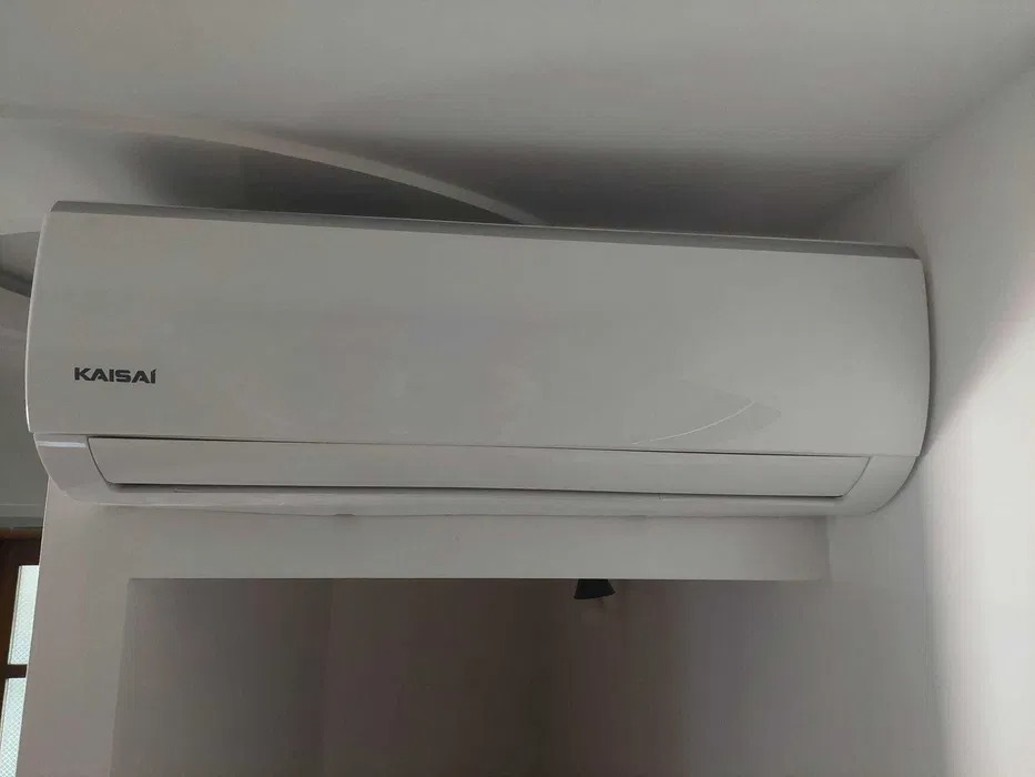 Biały klimatyzator Kaisai zamontowany na ścianie w pomieszczeniu, widoczne delikatne zaokrąglenia obudowy i cień na ścianie pod urządzeniem.
