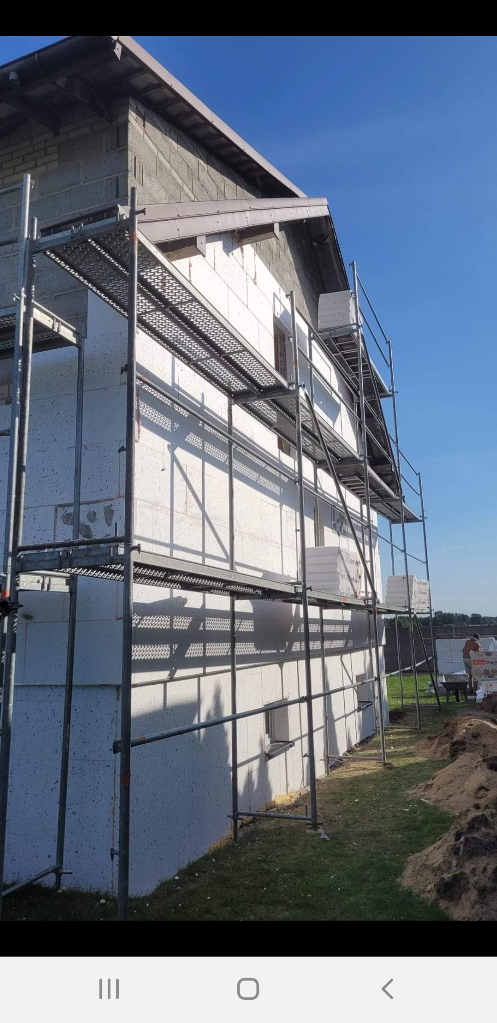 Budowa domu z białych bloczków silikatowych, widoczne rusztowania i częściowo wykonana elewacja, na górze budynku widoczny fragment ściany z szarego bloczka.