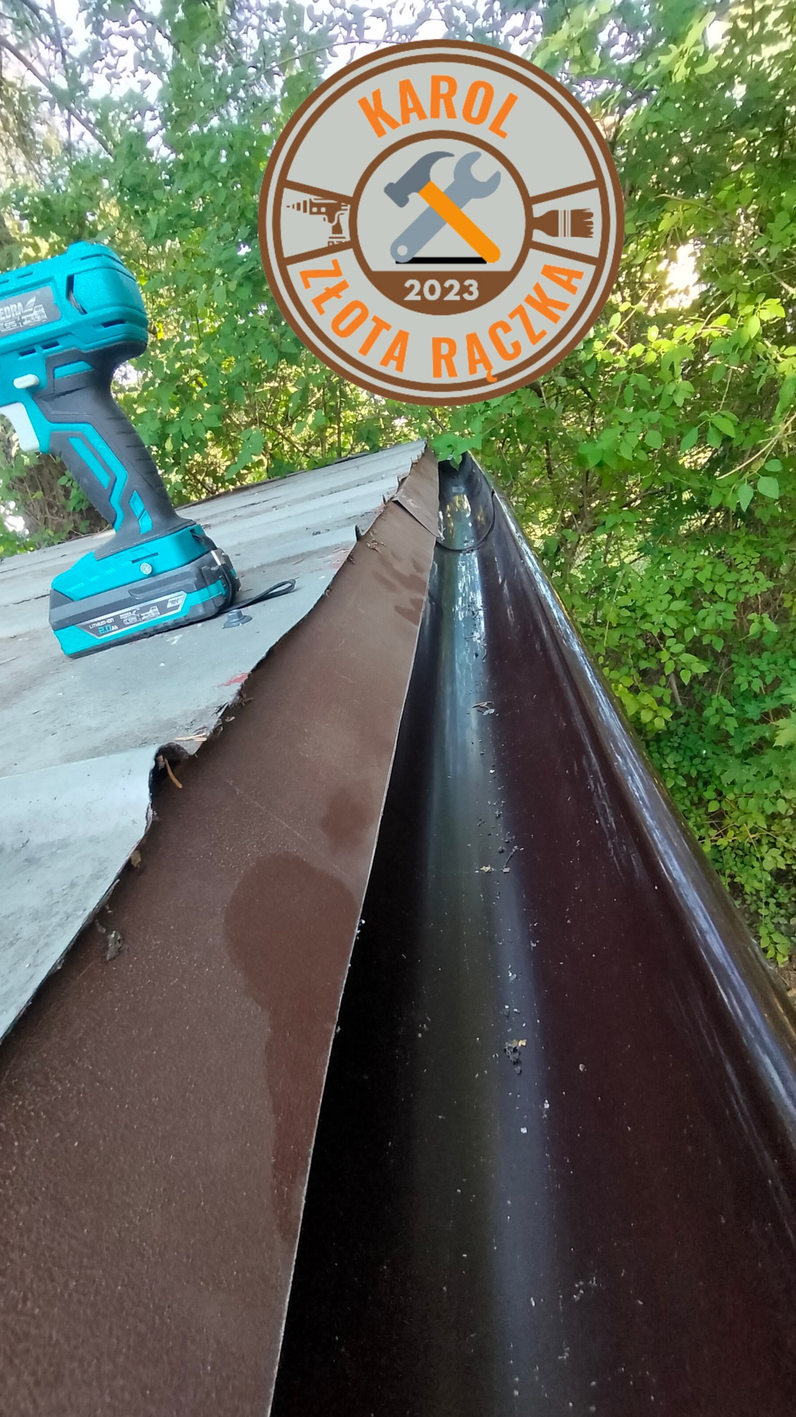 Brązowy system rynnowy na dachu, widoczna wkrętarka akumulatorowa i logo firmy 'Karol Złota Rączka 2023', tło z zielenią drzew.