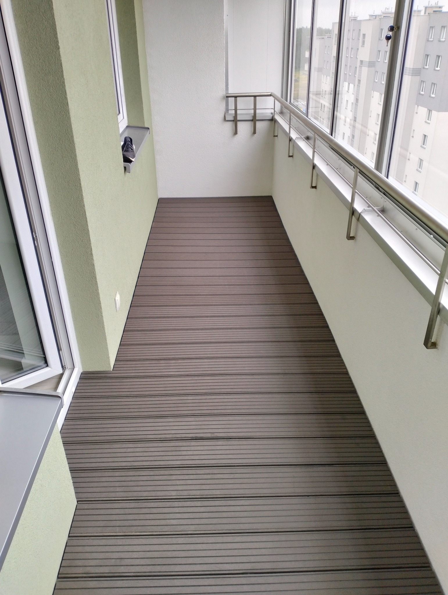 Nowoczesny balkon z deską kompozytową w Łapach. Widok na szare budynki przez okna. Minimalistyczne wykończenie, stalowa balustrada i jasne ściany.