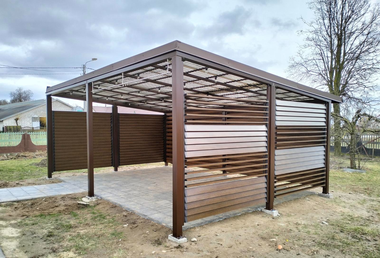 Nowoczesna pergola z brązowymi panelami i przezroczystym dachem, osłaniająca wybrukowany taras. Widok z zewnątrz, w tle trawnik i drzewa.