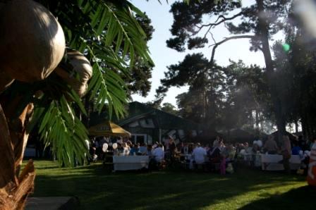 Plenerowa impreza firmowa z białymi stołami i dekoracjami w stylu tropikalnym, widok zza liści palmy.