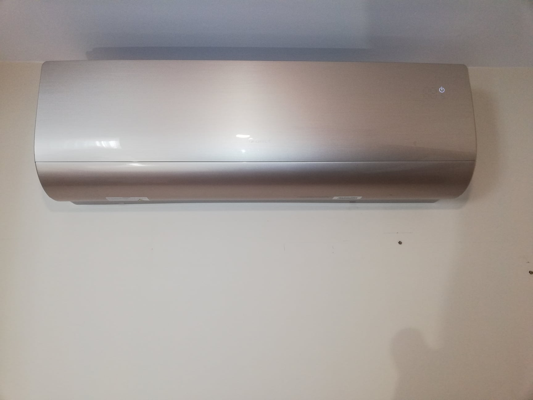 Nowoczesny, złoty klimatyzator ścienny zamontowany na białej ścianie, widoczny włącznik zasilania.