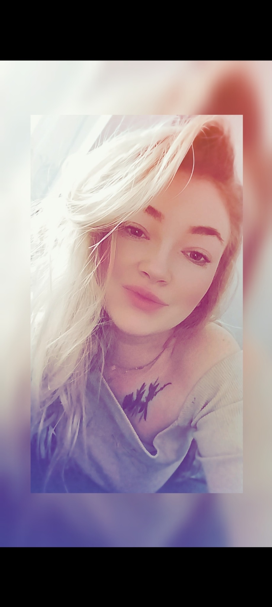 Portret kobiety z blond włosami, delikatnym makijażem i tatuażem na dekolcie, w miękkim, naturalnym świetle.